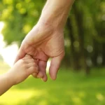 Adult holding child_s hand in green field